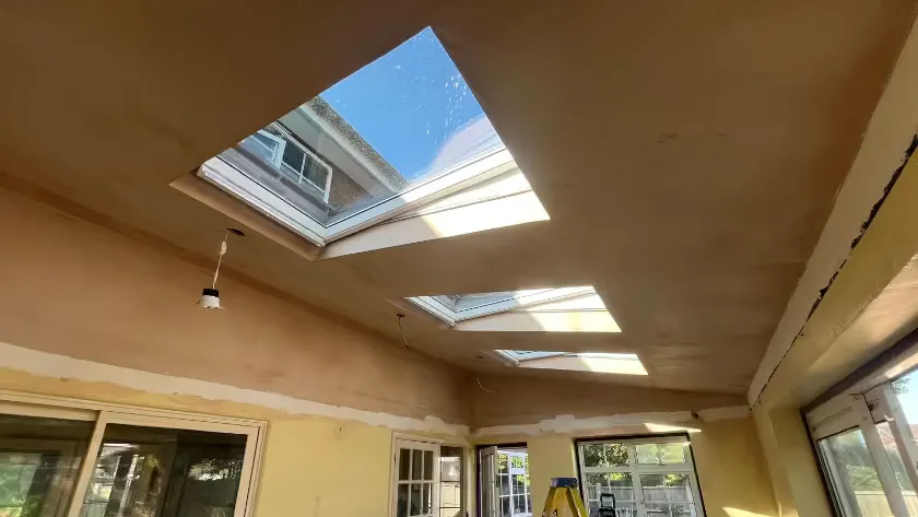 Completed vaulted ceiling with three Velux windows letting in blue sky, the plaster finished and the light fittings still to go up