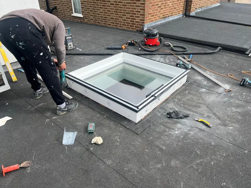 Installer fitting a new Velux solar-powered roof window into the prepared opening on a flat roof in Esher