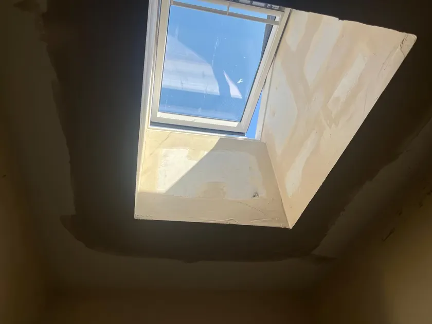 New Velux solar powered roof window open above the plastered light shaft, with sunlight streaming into the hallway below
