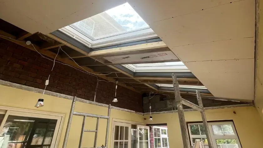 Three Velux windows fitted into the roof slope during the work, with the new ceiling being boarded around them and scaffold towers below