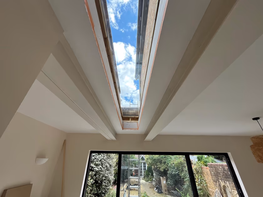 Finished long flat glass rooflight in a new rear extension ceiling, with blue sky above and garden doors below