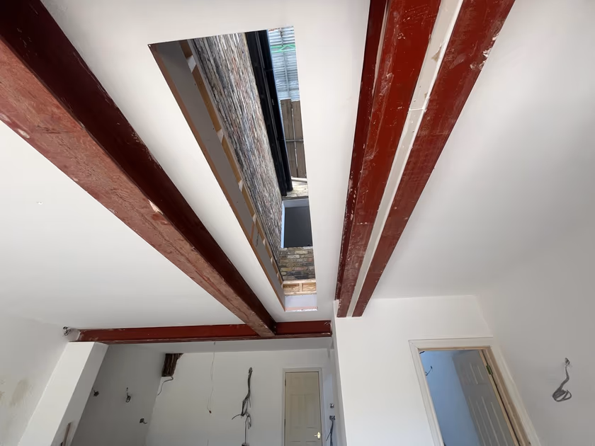 Rooflight opening formed in the extension ceiling between red painted steel beams, open to the sky
