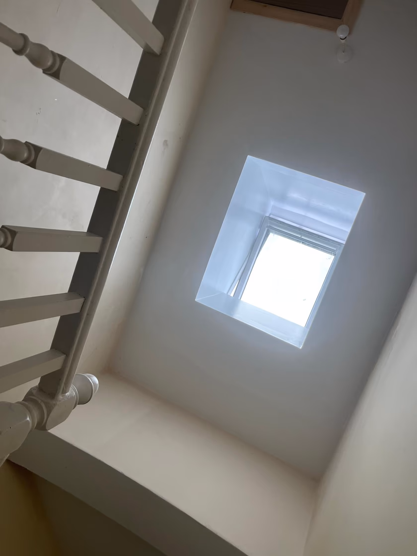 The finished, painted light shaft seen from the stairs, flooding the hallway with natural light