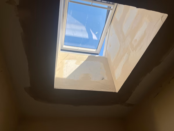 New Velux solar powered roof window ajar above the plastered light shaft, with sunlight streaming into the hallway below