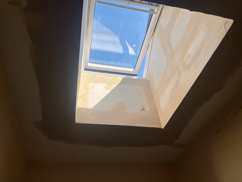 New Velux solar powered roof window ajar above the plastered light shaft, with sunlight streaming into the hallway below
