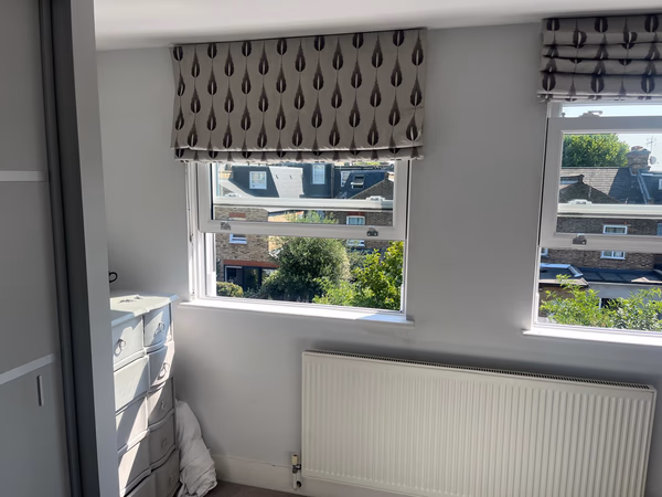 Two new white sash windows fitted in a Southfields bedroom, with patterned blinds above and views over neighbouring gardens