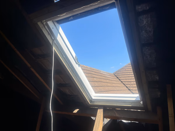 New electric Velux roof window fitted into the pitched roof of a Surbiton loft, with blue sky and neighbouring rooftops beyond