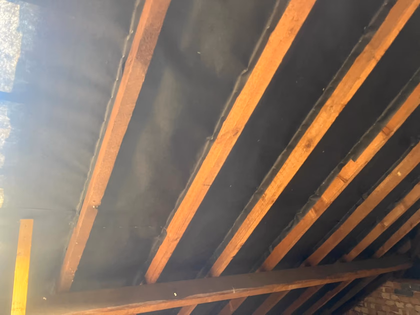 The unconverted Surbiton loft before work, with bare timber rafters and dark roofing membrane and no natural light