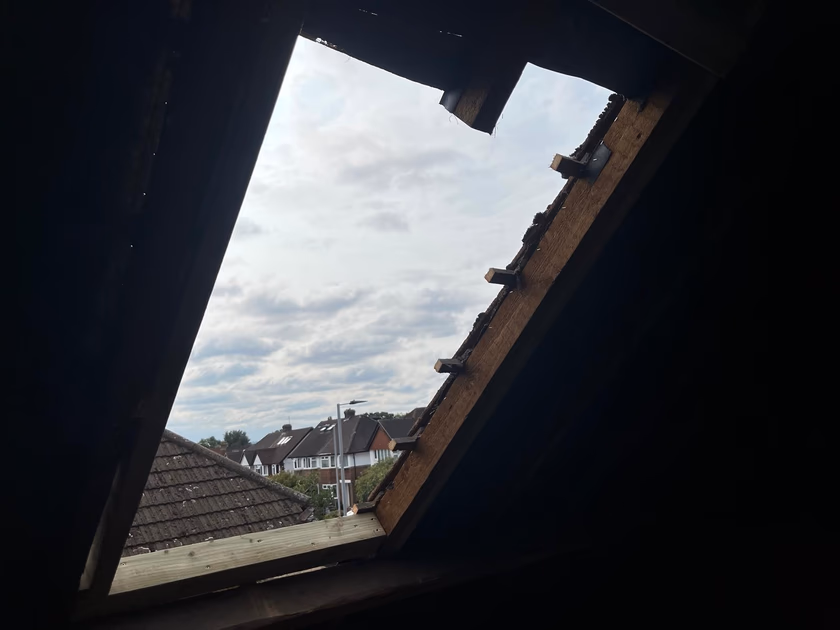 Opening cut into the pitched roof with trimmed rafters and new timber framing, looking out over neighbouring houses
