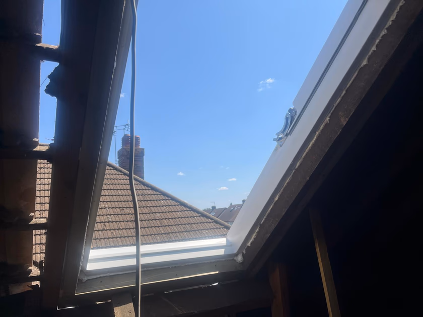 New white Velux window frame being fitted into the prepared roof opening, seen from inside the loft