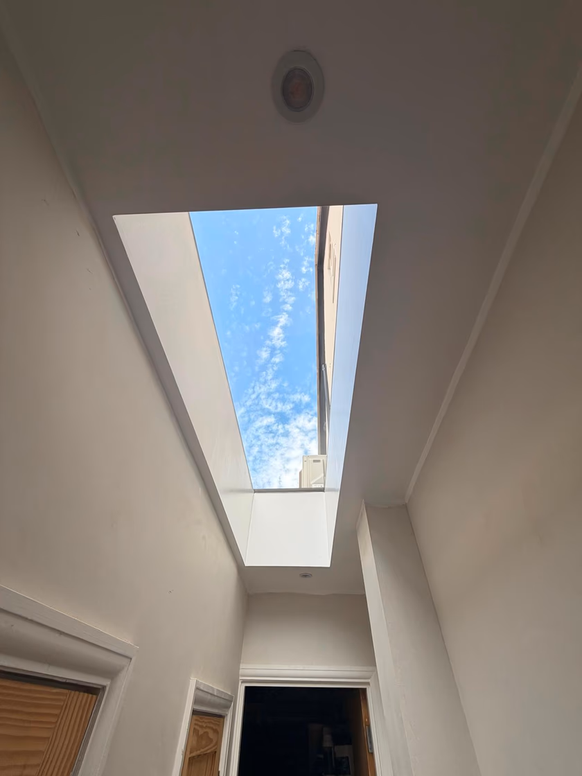 The finished white plastered light shaft and flat glass rooflight brightening the hallway below